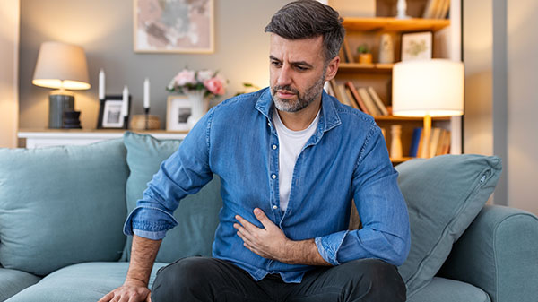 Terrible stomachache. Frustrated handsome young man hugging his belly and keeping eyes closed while lying on the couch at home
