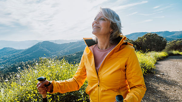 Active senior woman hiking on outdoor trail using trekking poles